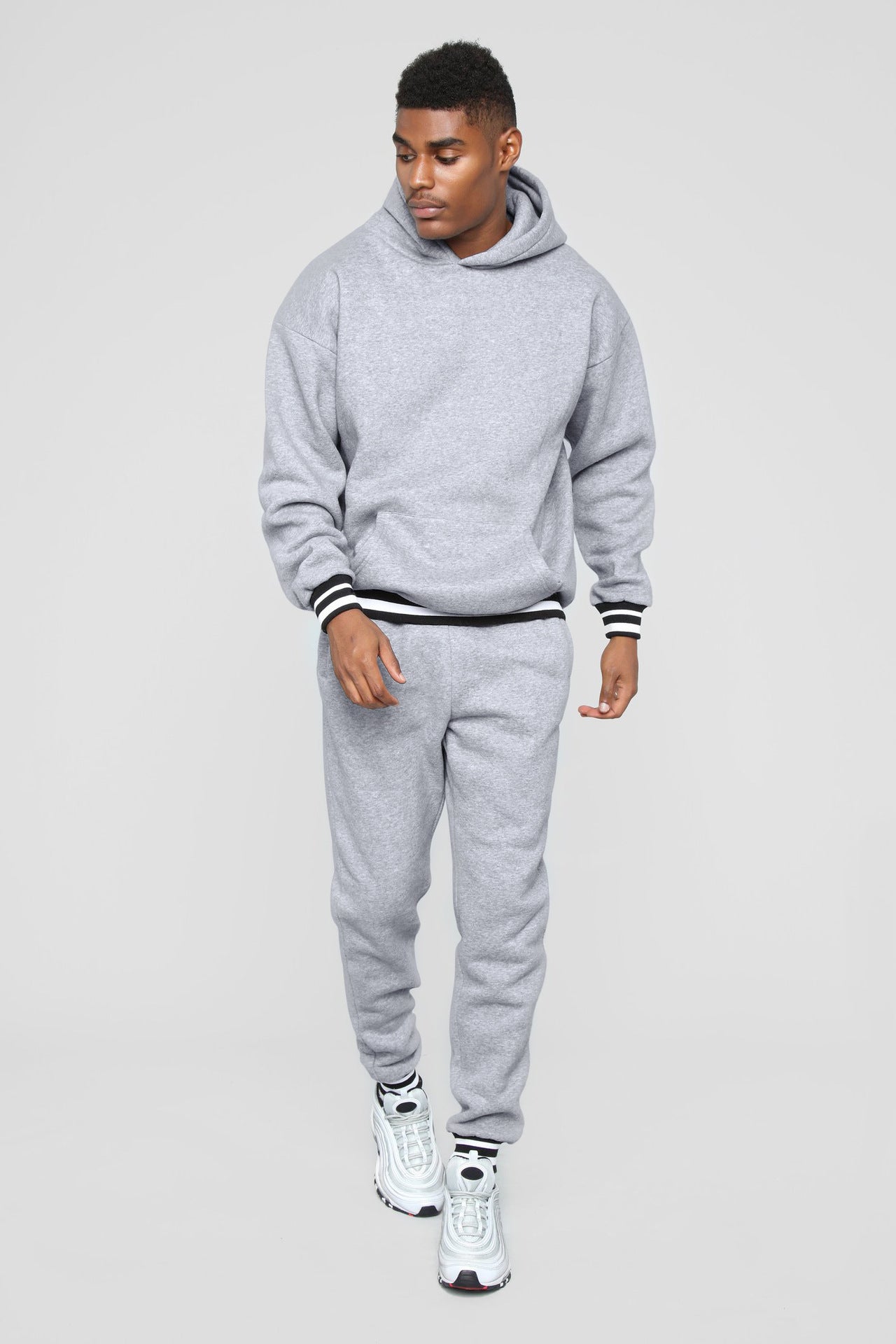 Man wearing a gray hoodie and matching sweatpants with white sneakers on a plain background