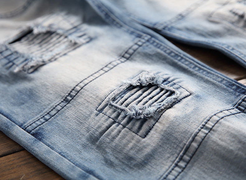 Close-up of light blue distressed denim jeans with ripped patches and ribbed detailing on wooden surface