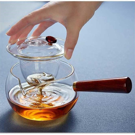 Hand lifting glass lid from transparent glass teapot with wooden handle and amber tea inside