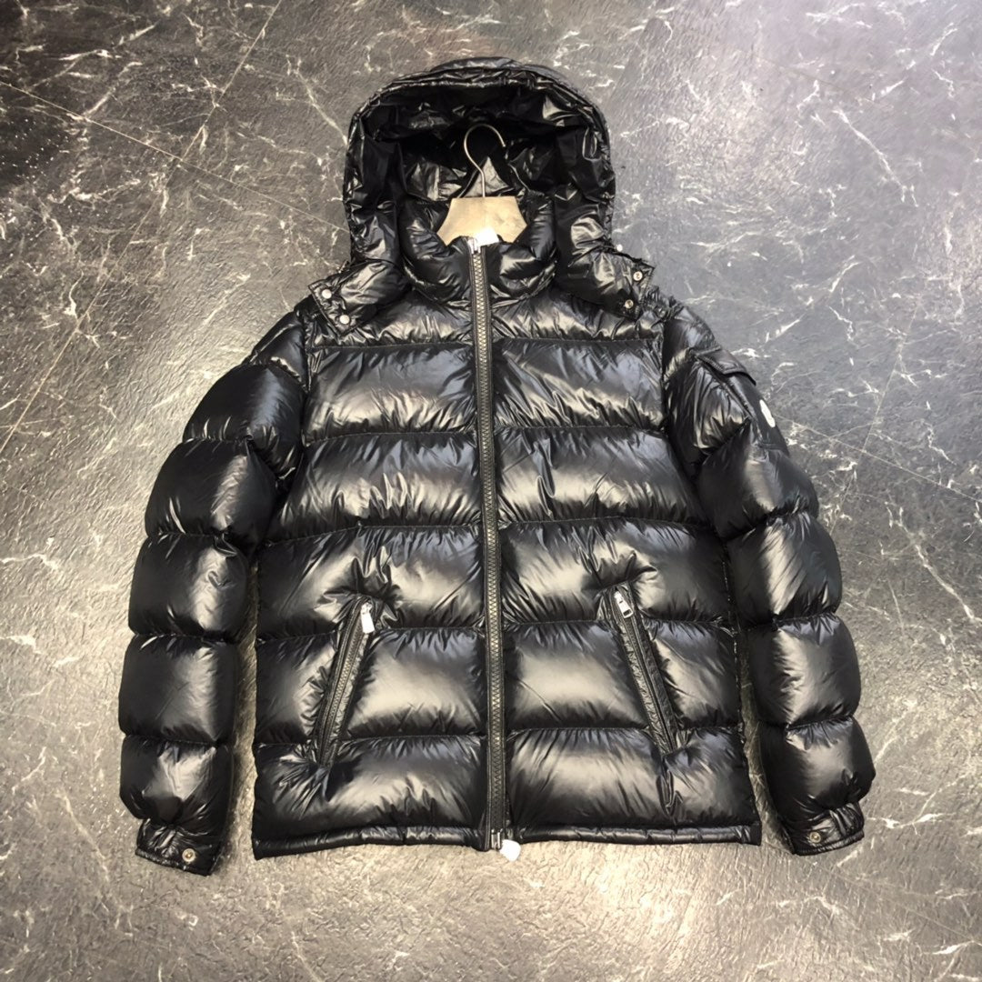 Black shiny puffer jacket with hood, zippered pockets, and quilted design on marble floor