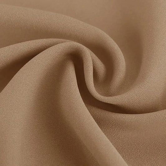 Close-up of smooth tan fabric with fine texture, softly folded in a swirl pattern