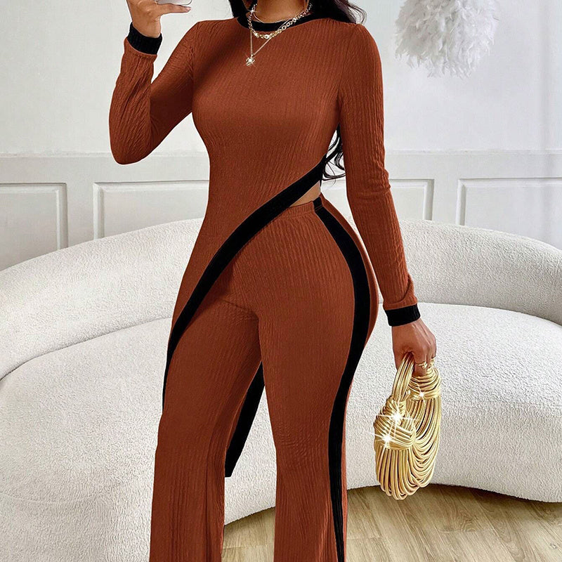Woman wearing rust-colored ribbed jumpsuit with black accents holding gold woven handbag indoors