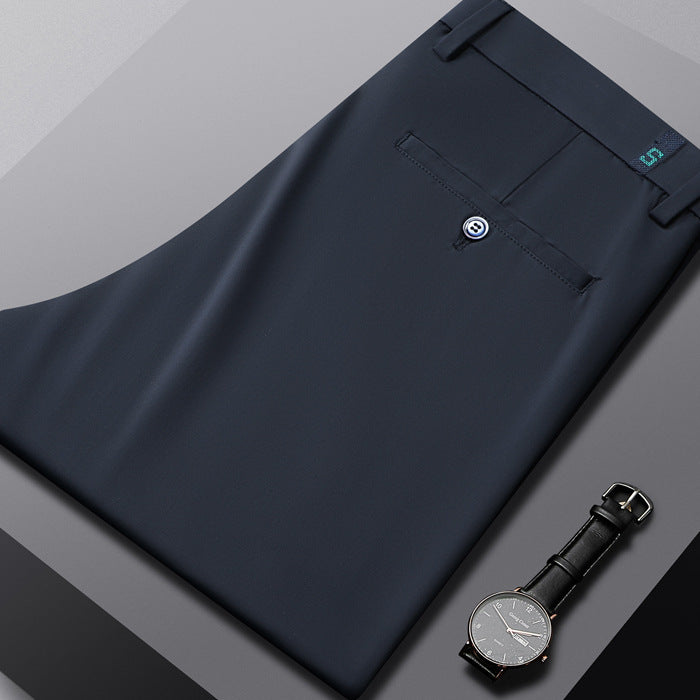 Folded navy blue dress pants with a buttoned back pocket beside a black leather strap watch on gray background