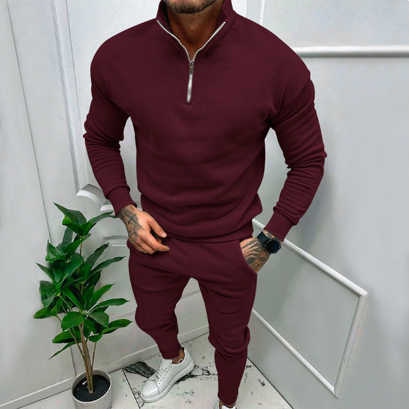 Man wearing maroon quarter-zip sweatshirt and matching joggers with white sneakers standing indoors near potted plant