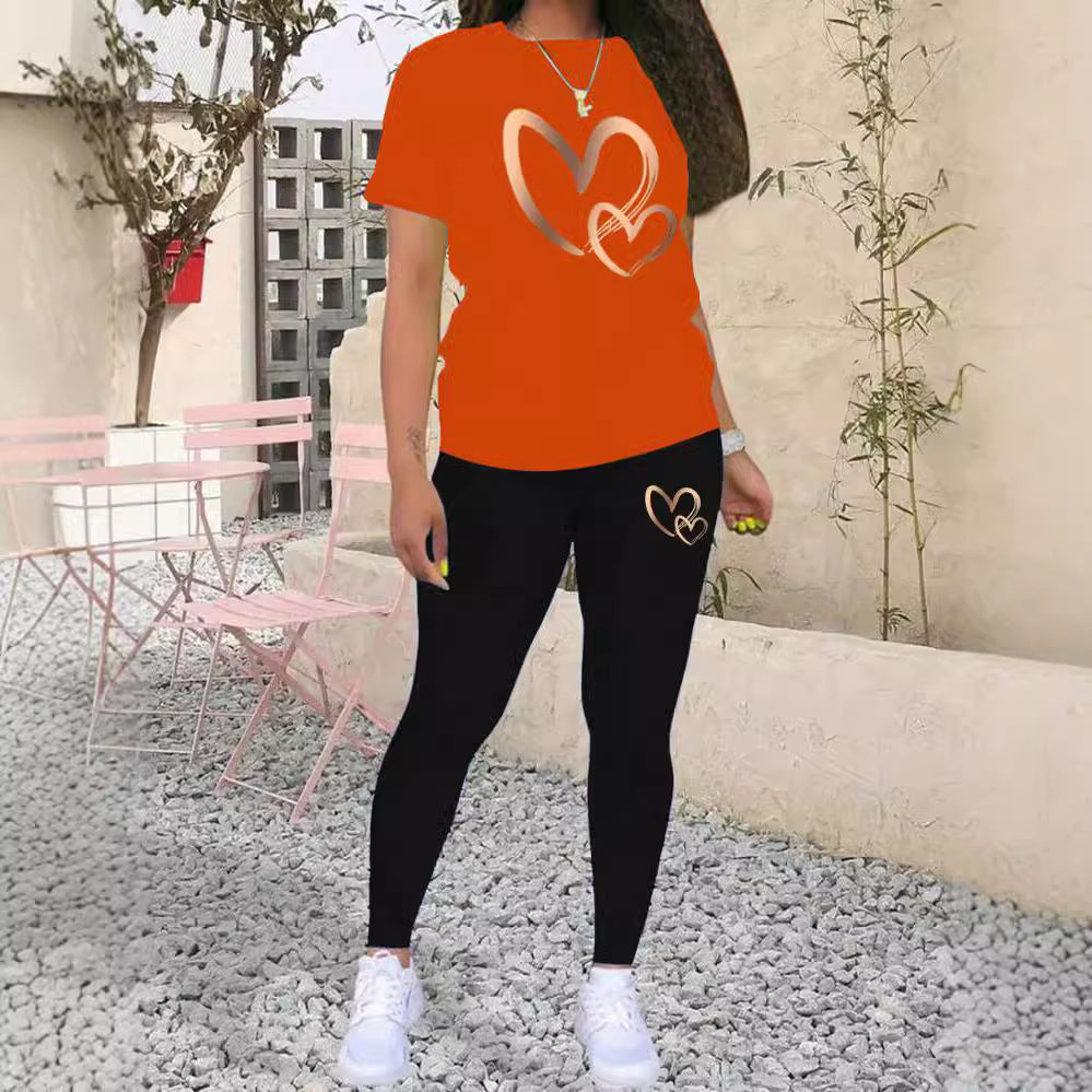 Woman wearing orange T-shirt and black leggings with heart designs, standing on gravel patio