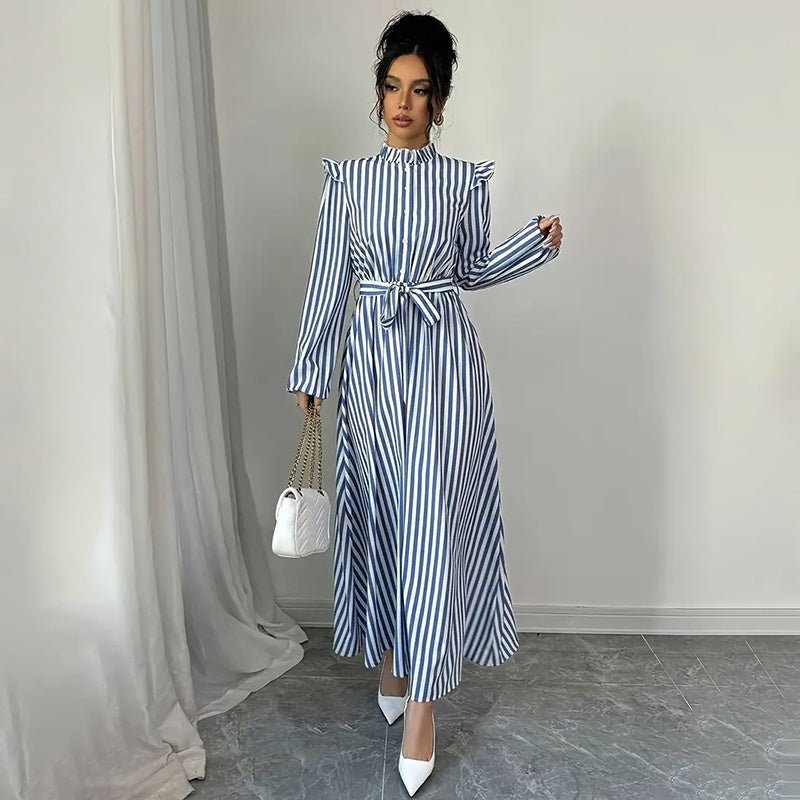 Woman wearing blue and white striped long sleeve maxi dress with stand collar, waist tie, and white heels