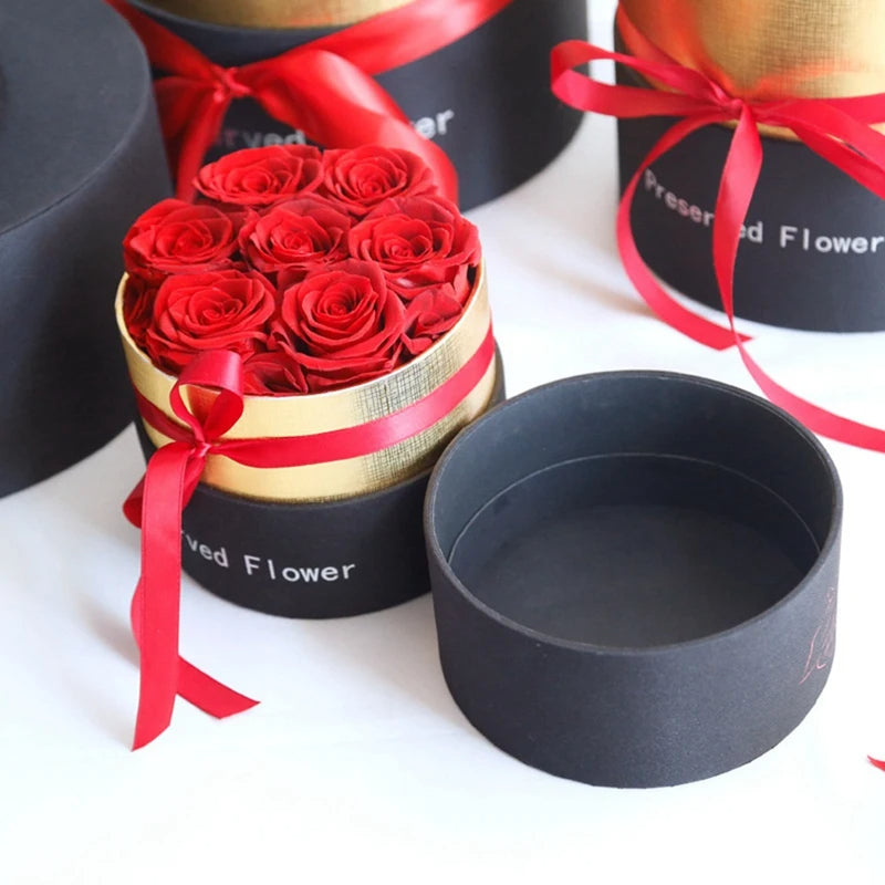 Round black gift box with red roses and red ribbon bow on gold wrap, surrounded by other black boxes