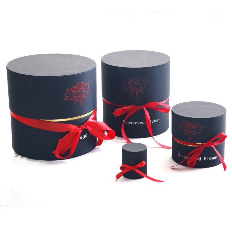 Four black round gift boxes with red ribbon bows and rose design, labeled for preserved flowers