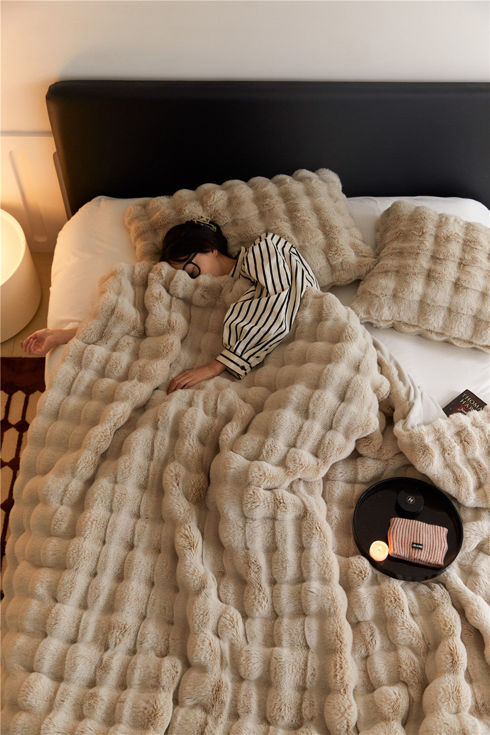 Person sleeping on bed with soft beige faux fur blanket and pillows in cozy bedroom