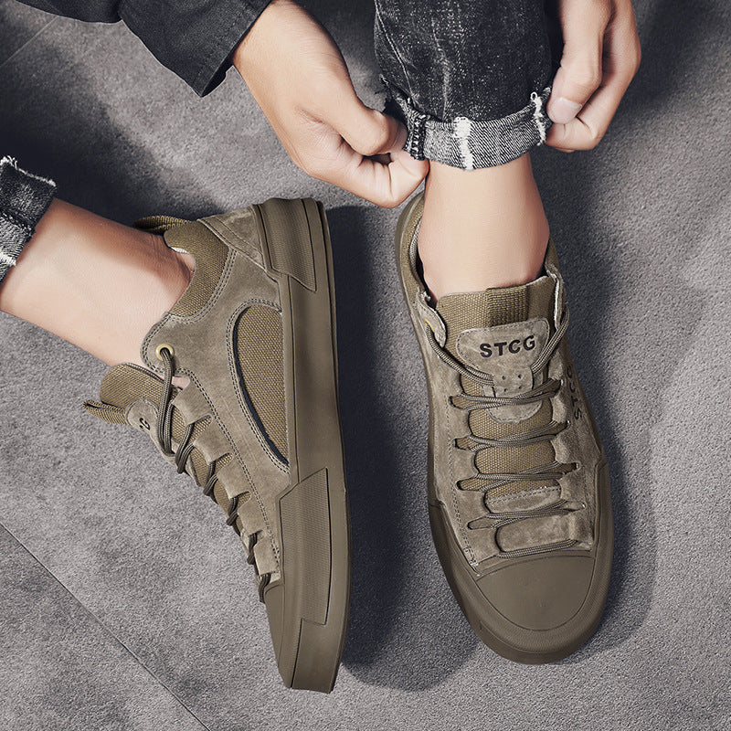 Pair of olive green STCG casual sneakers worn with rolled-up black jeans on gray floor