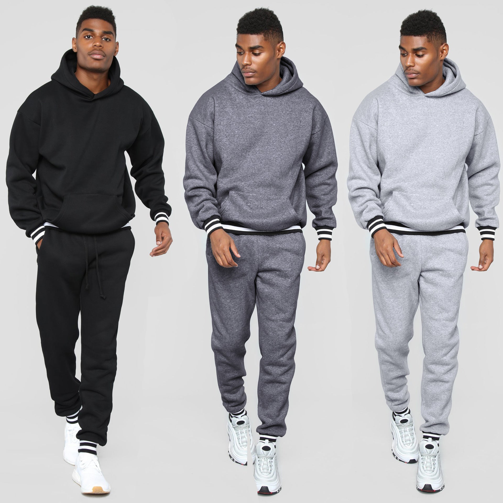 Man modeling black, dark gray, and light gray hooded sweatshirts and matching joggers with striped cuffs.