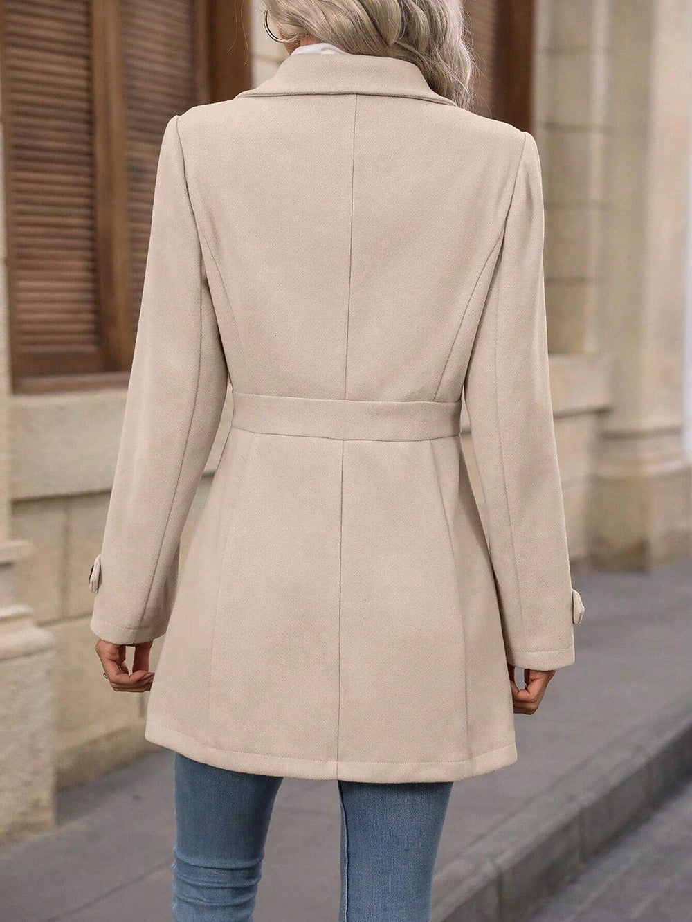 Back view of woman wearing beige belted wool coat with tailored seams and long sleeves on city street