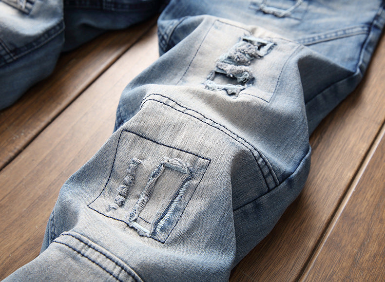 Close-up of light blue distressed denim jeans with frayed patches on wooden floor