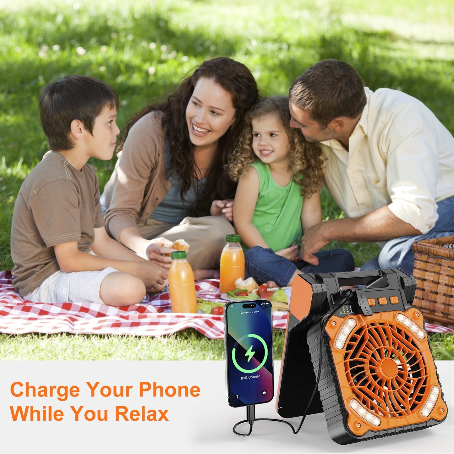 Family picnic outdoors with portable fan charging a phone, relaxing on a red checkered blanket