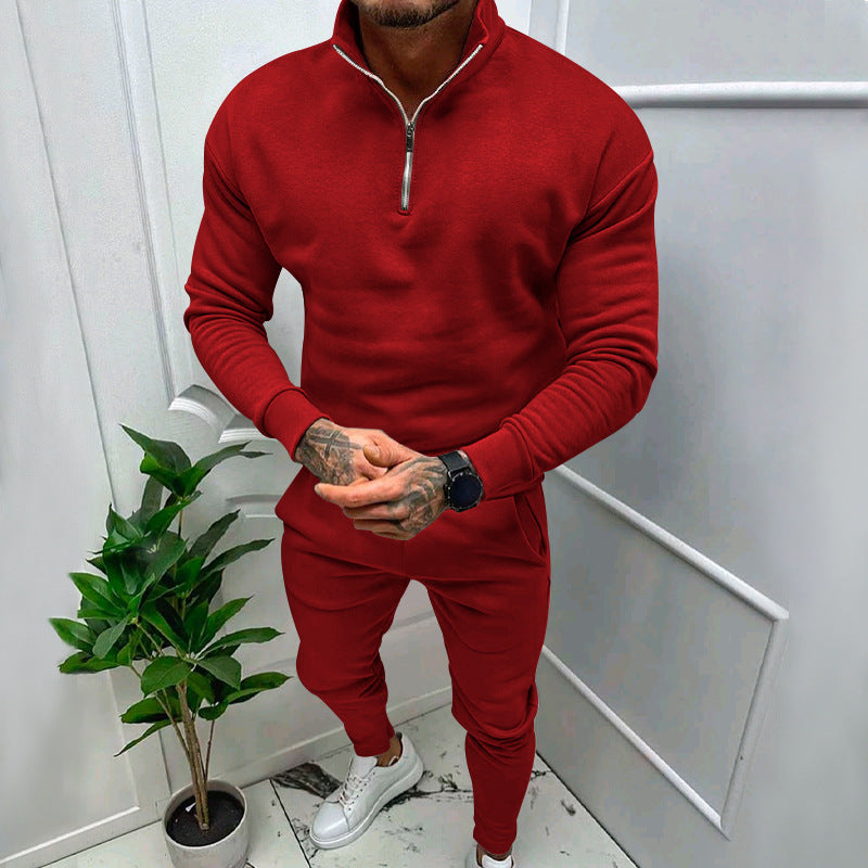 Man wearing a red zip-up sweatshirt and matching joggers with white sneakers, standing indoors