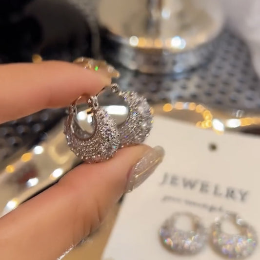 Hand holding sparkling silver hoop earrings with rhinestone details over jewelry display