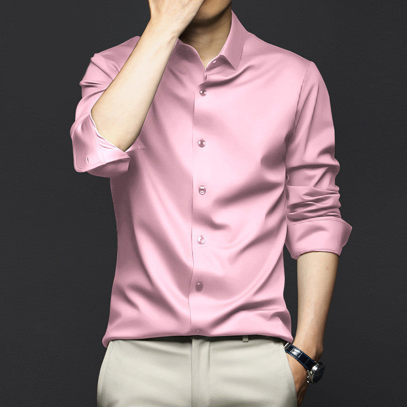 Man wearing a pink button-up shirt with rolled sleeves and beige pants against dark background