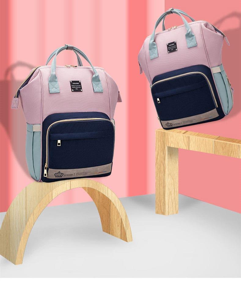 Pink and navy blue backpack with light blue handles displayed on wooden stand and table against pink background
