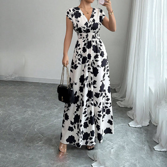 Woman wearing white maxi dress with black floral print, holding black handbag with gold chain