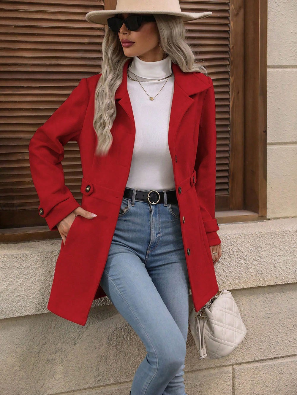 Woman wearing red coat, white turtleneck, light blue jeans, beige hat, black sunglasses, and holding white quilted purse