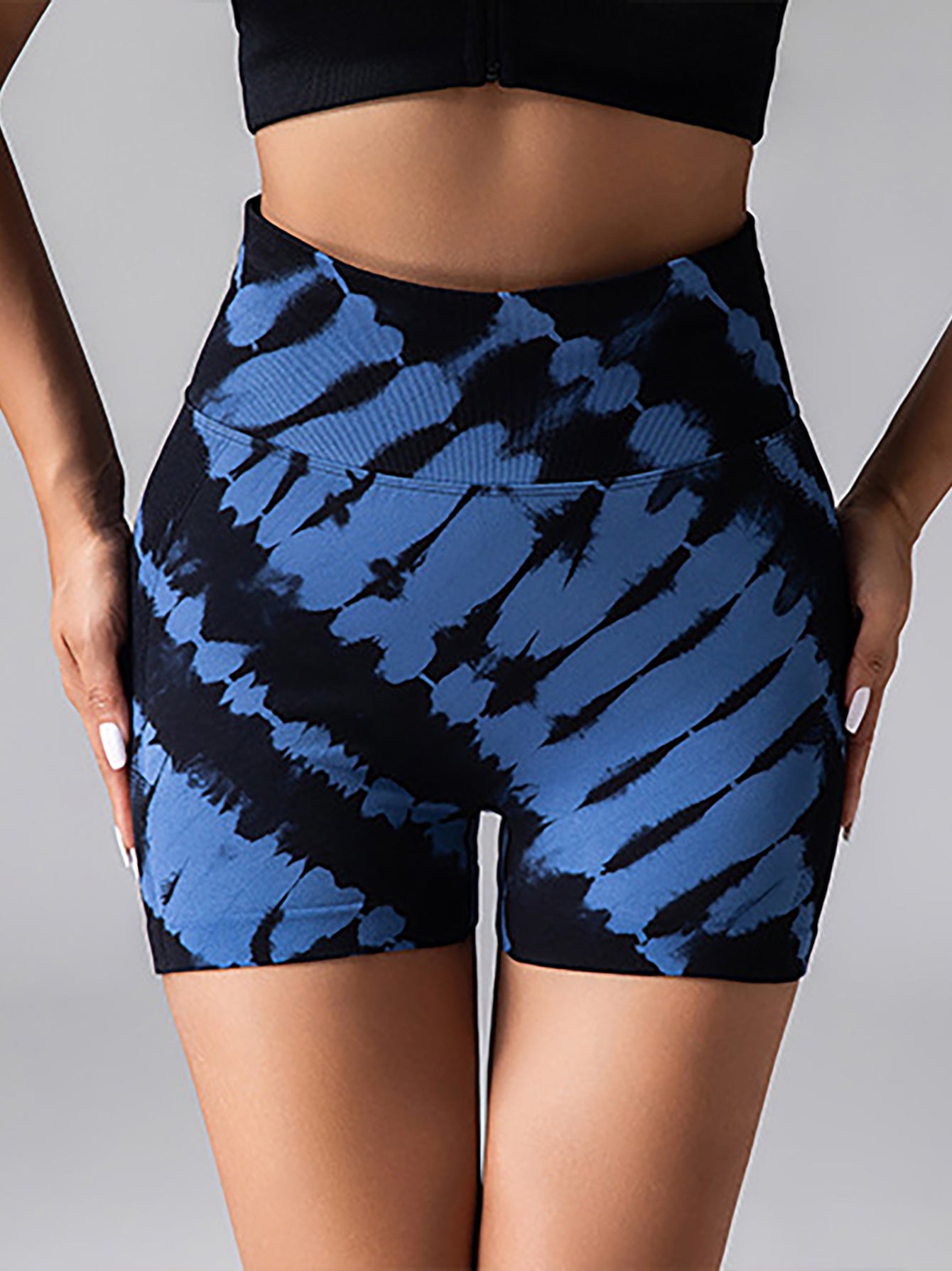 Close-up of woman wearing high-waisted blue and black tie-dye workout shorts and black crop top