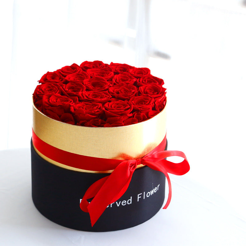 Round black and gold flower box filled with vibrant red preserved roses tied with a red satin ribbon