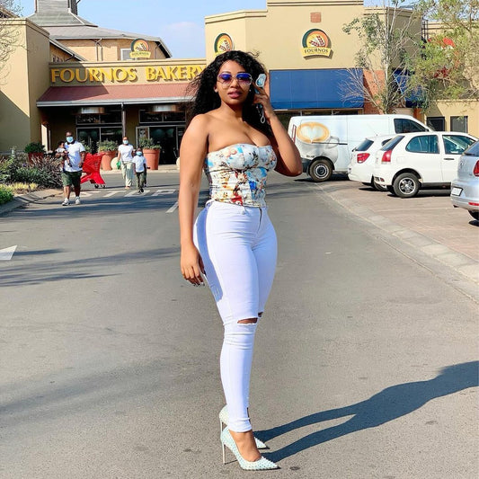 Woman in white ripped jeans and patterned strapless top posing outside Fournos Bakery on sunny day