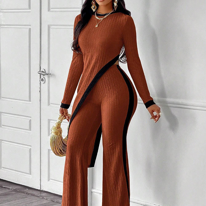 Woman wearing a rust brown ribbed long-sleeve jumpsuit with black accents, holding a gold handbag