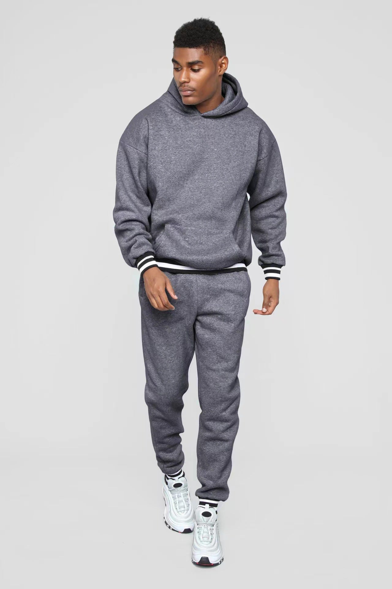 Young man wearing a gray hoodie and matching sweatpants with white sneakers on a light background