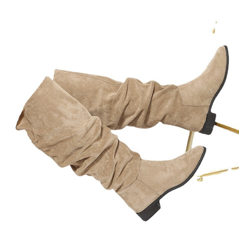 Pair of beige suede slouchy knee-high boots with low black heels on white background