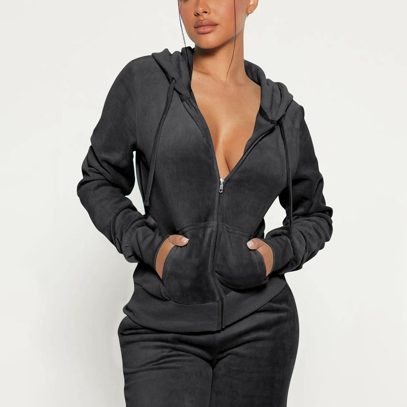 Woman wearing black zip-up hoodie and matching jogger pants with hands in pockets on white background