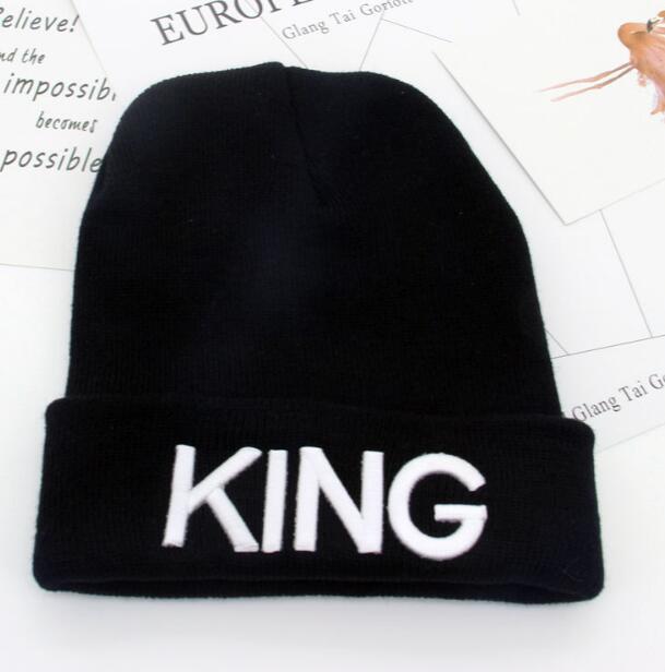Black knit beanie hat with white embroidered text 'KING' on cuff, placed on white papers background