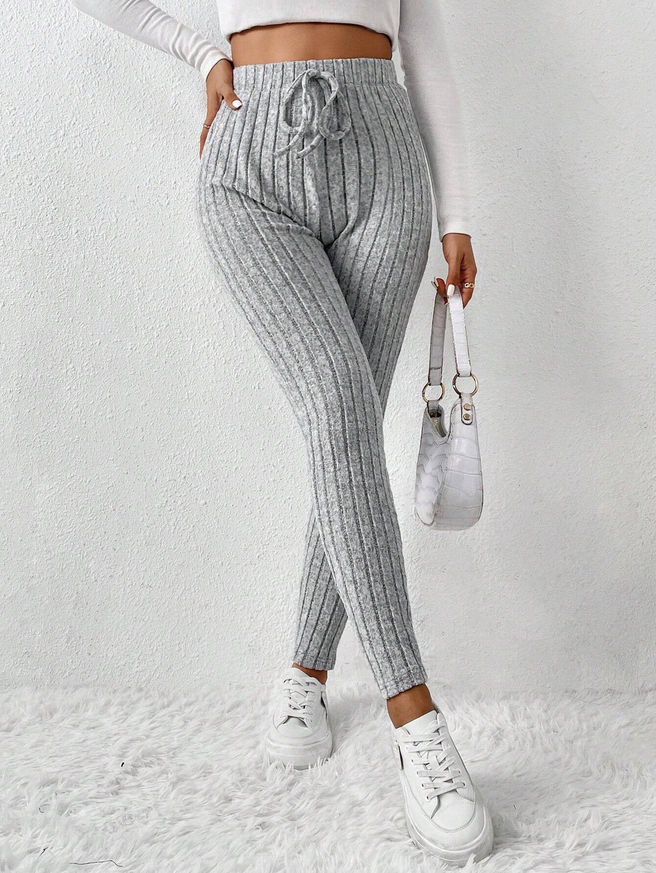 Woman wearing gray ribbed knit pants with drawstring, white crop top, white sneakers, holding white handbag