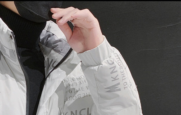Person wearing light gray MNCL jacket with text details on sleeve and chest, black turtleneck visible