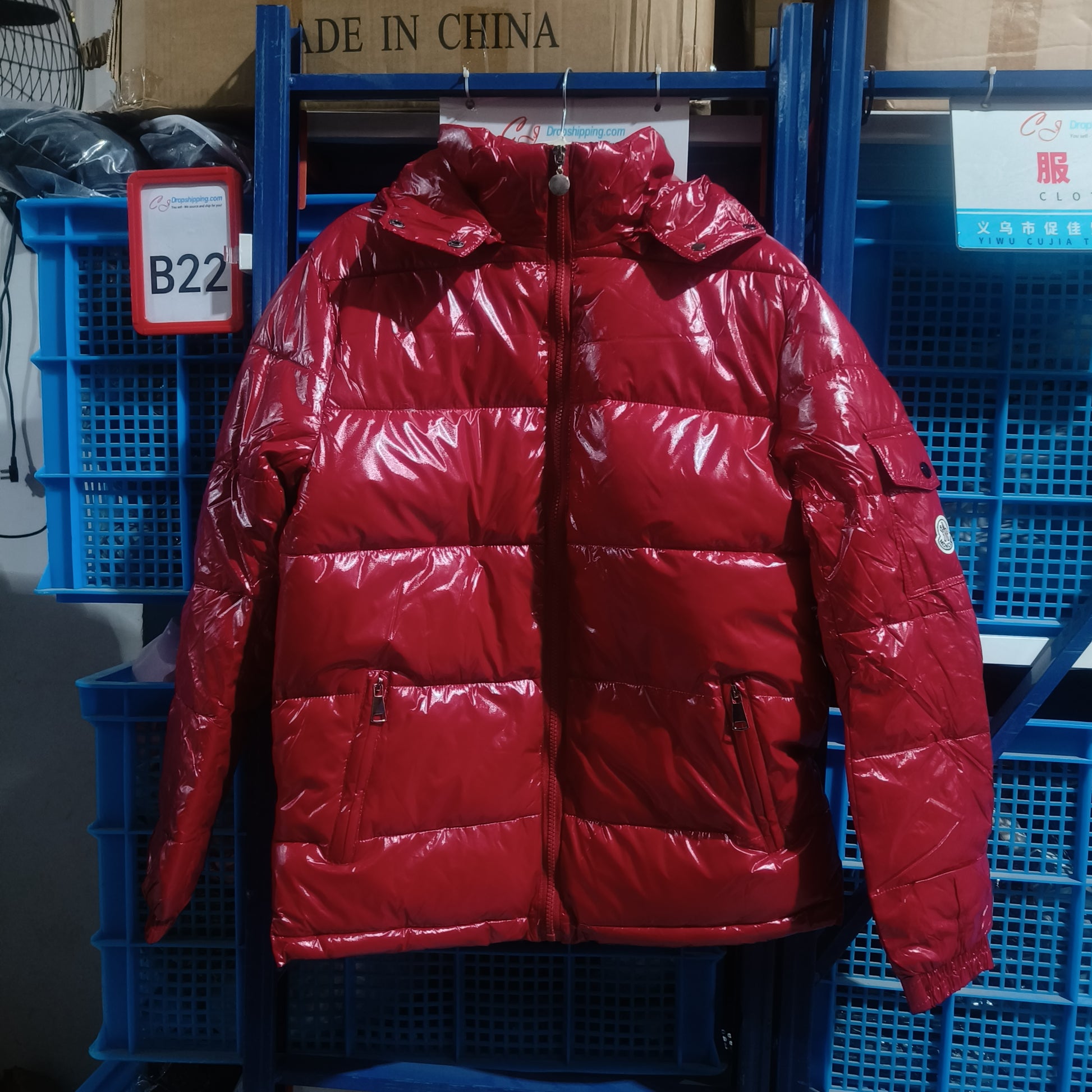 Glossy red puffer jacket with zipper pockets hanging on blue shelves in a warehouse
