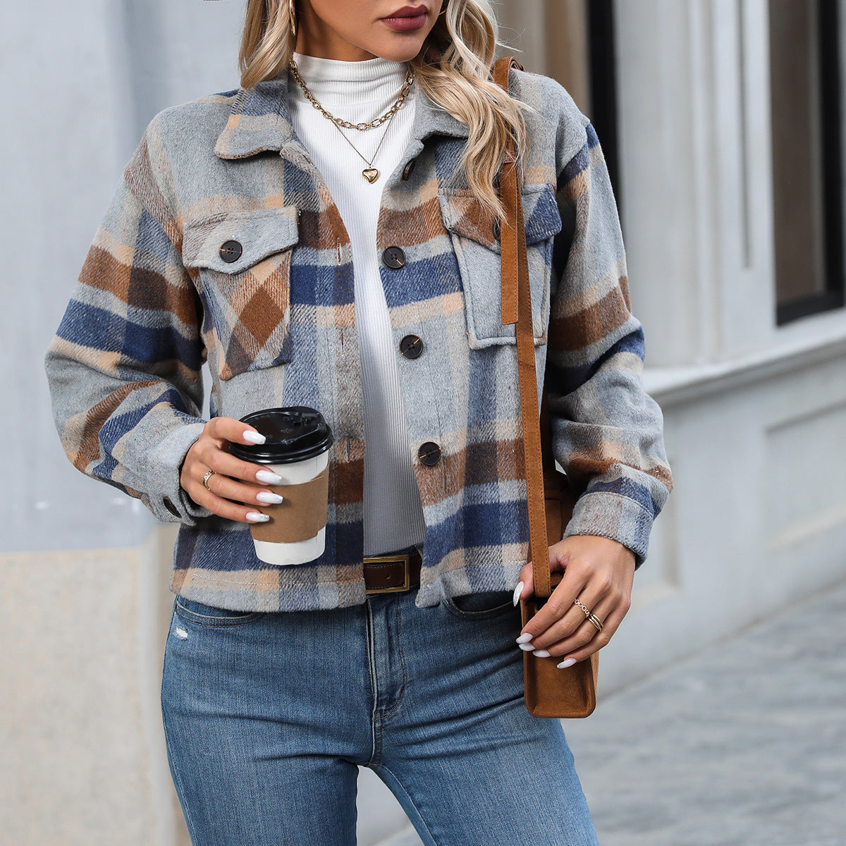 Woman wearing blue and brown plaid button-up jacket with white turtleneck and jeans, holding coffee cup