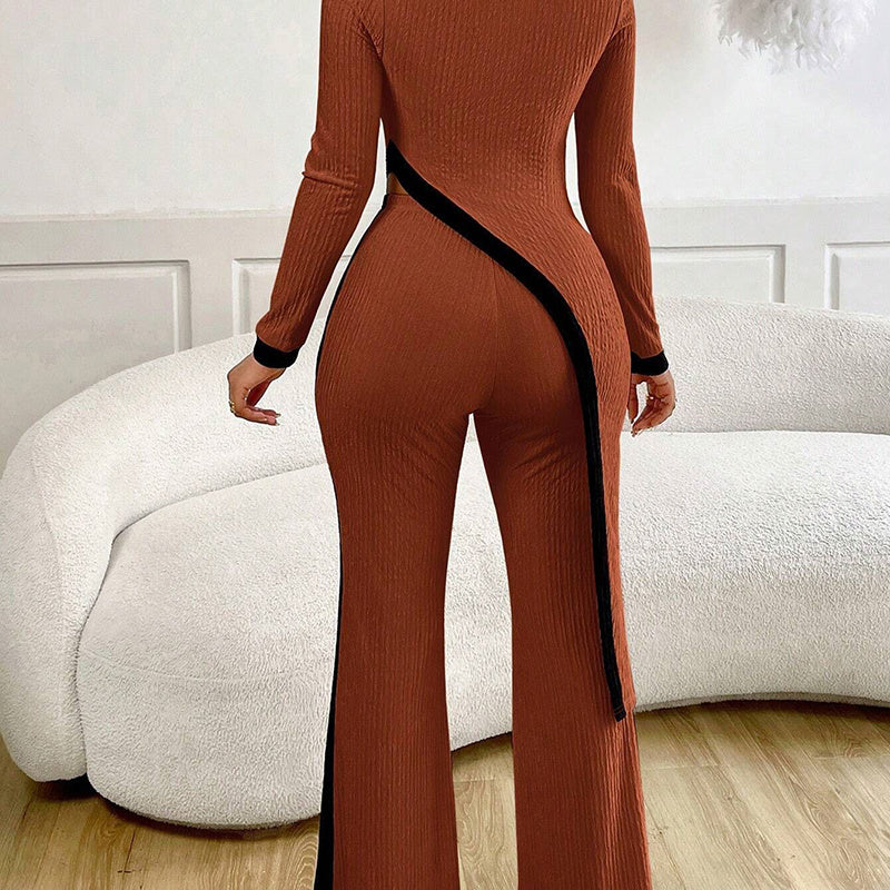 Back view of woman wearing rust ribbed knit jumpsuit with black trim, standing in modern living room