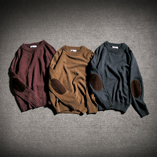 Three cozy knit sweaters in burgundy, brown, and dark gray with elbow patches laid on carpet