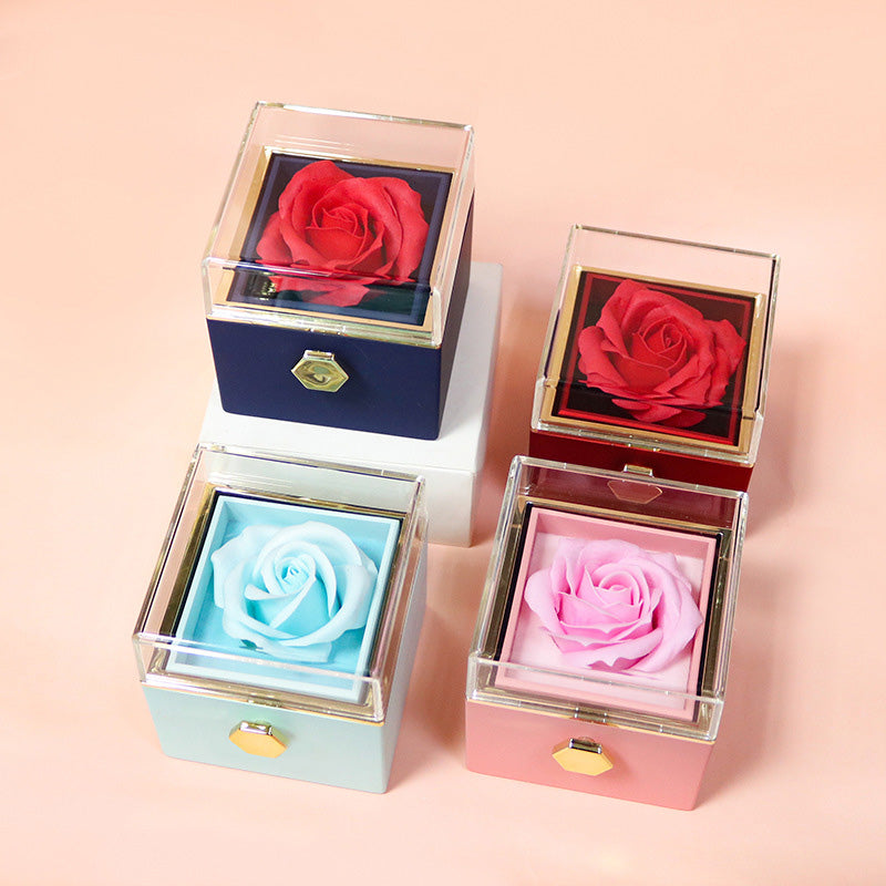 Four square gift boxes with clear lids, each containing a preserved rose in red, pink, and blue colors