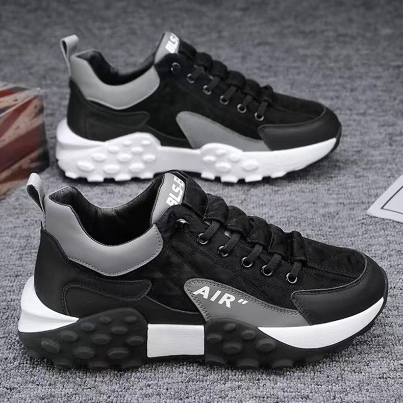 Black and gray athletic sneakers with thick white and black textured soles on a gray carpet