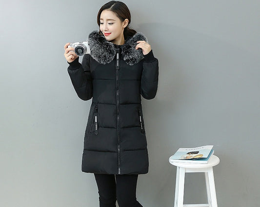 Woman wearing black winter coat with fur collar holding a camera against gray background