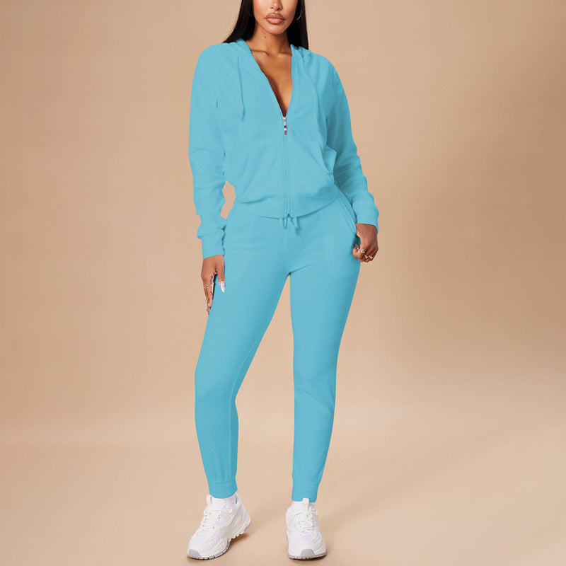 Woman wearing light blue zip-up hoodie and matching joggers with white sneakers on beige background