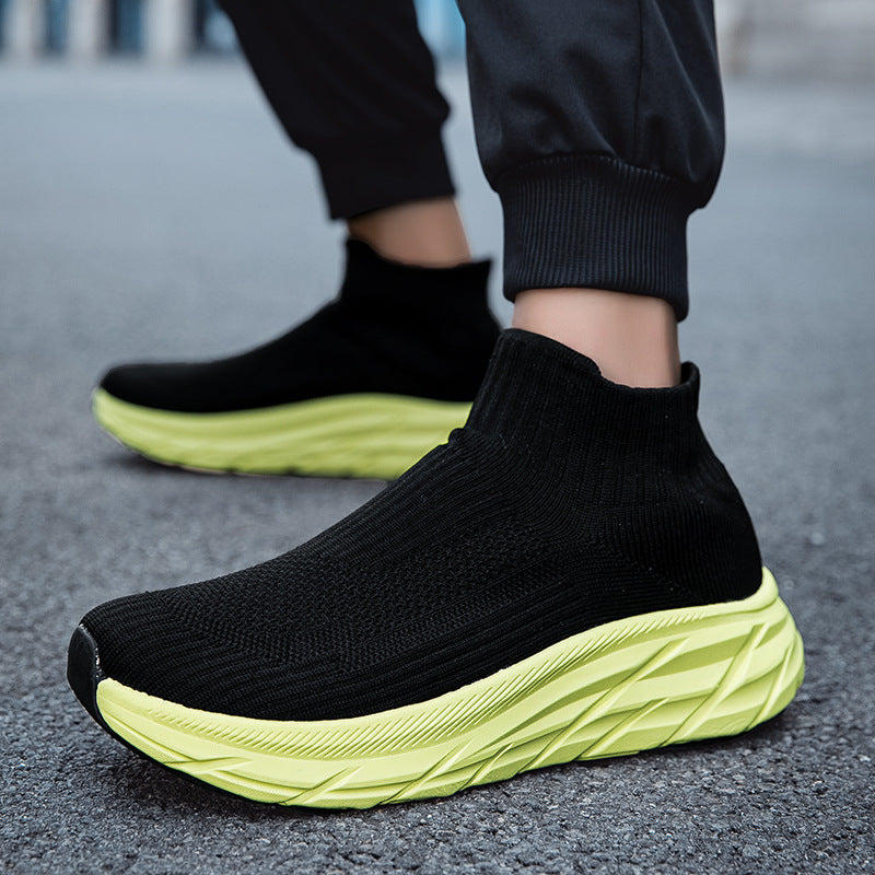 Black sock-style sneakers with textured neon green thick soles on asphalt surface