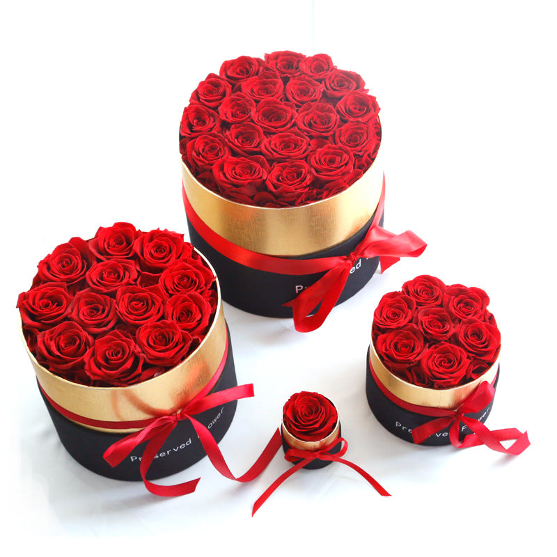 Four round black and gold boxes with red preserved roses, decorated with red ribbons on a white background
