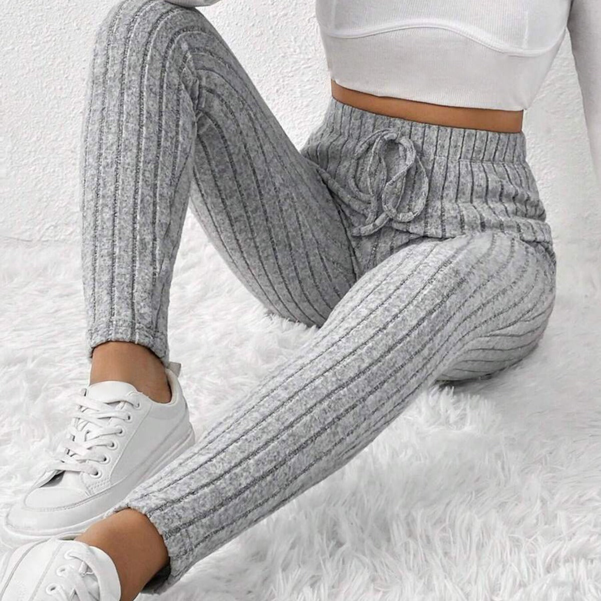 Woman wearing gray ribbed knit lounge pants with drawstring and white sneakers on white fluffy rug