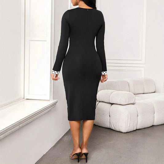 Woman in black midi dress with long sleeves and polka dot cuffs, standing in modern living room