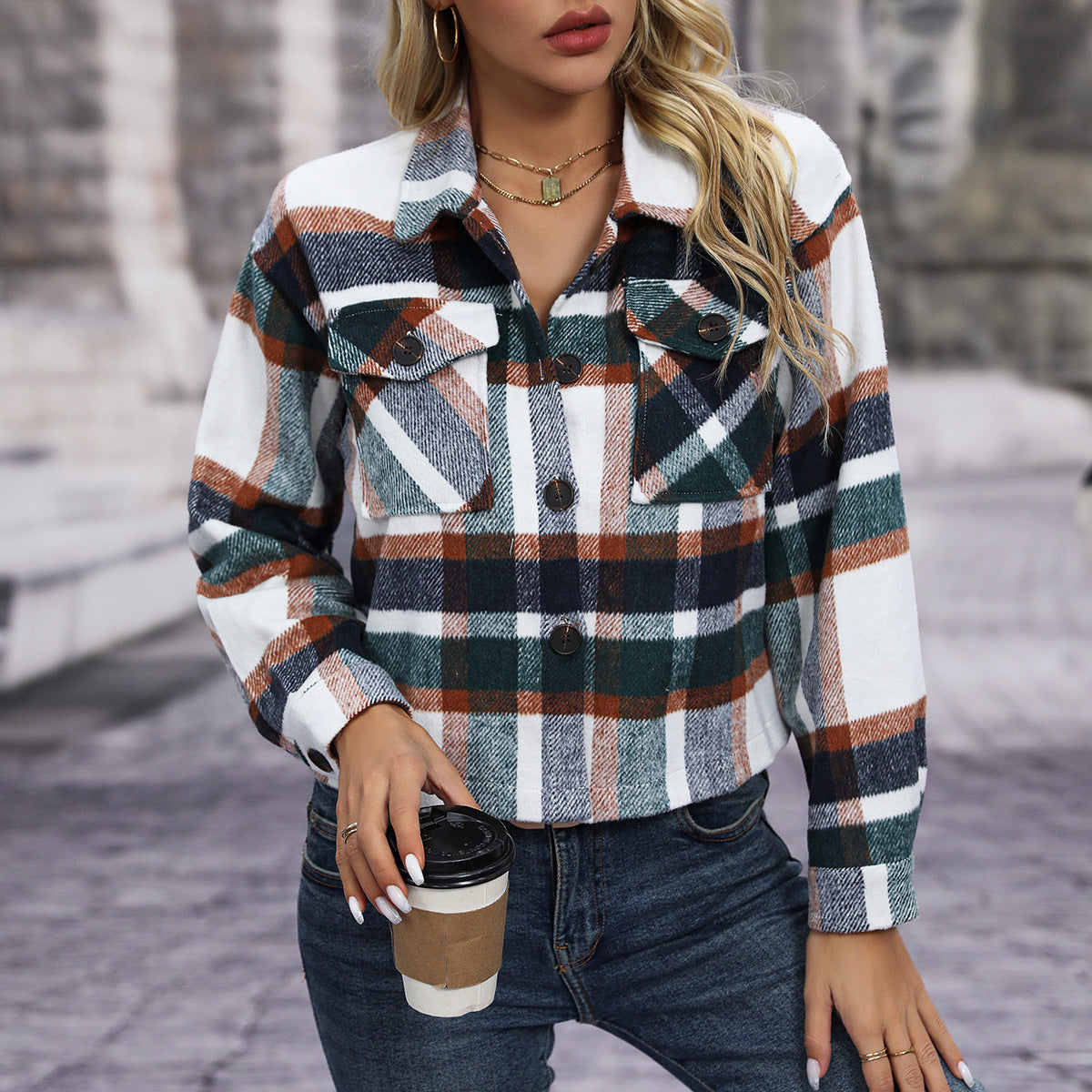 Woman wearing a plaid button-up wool shirt holding a coffee cup, styled with layered necklaces and jeans