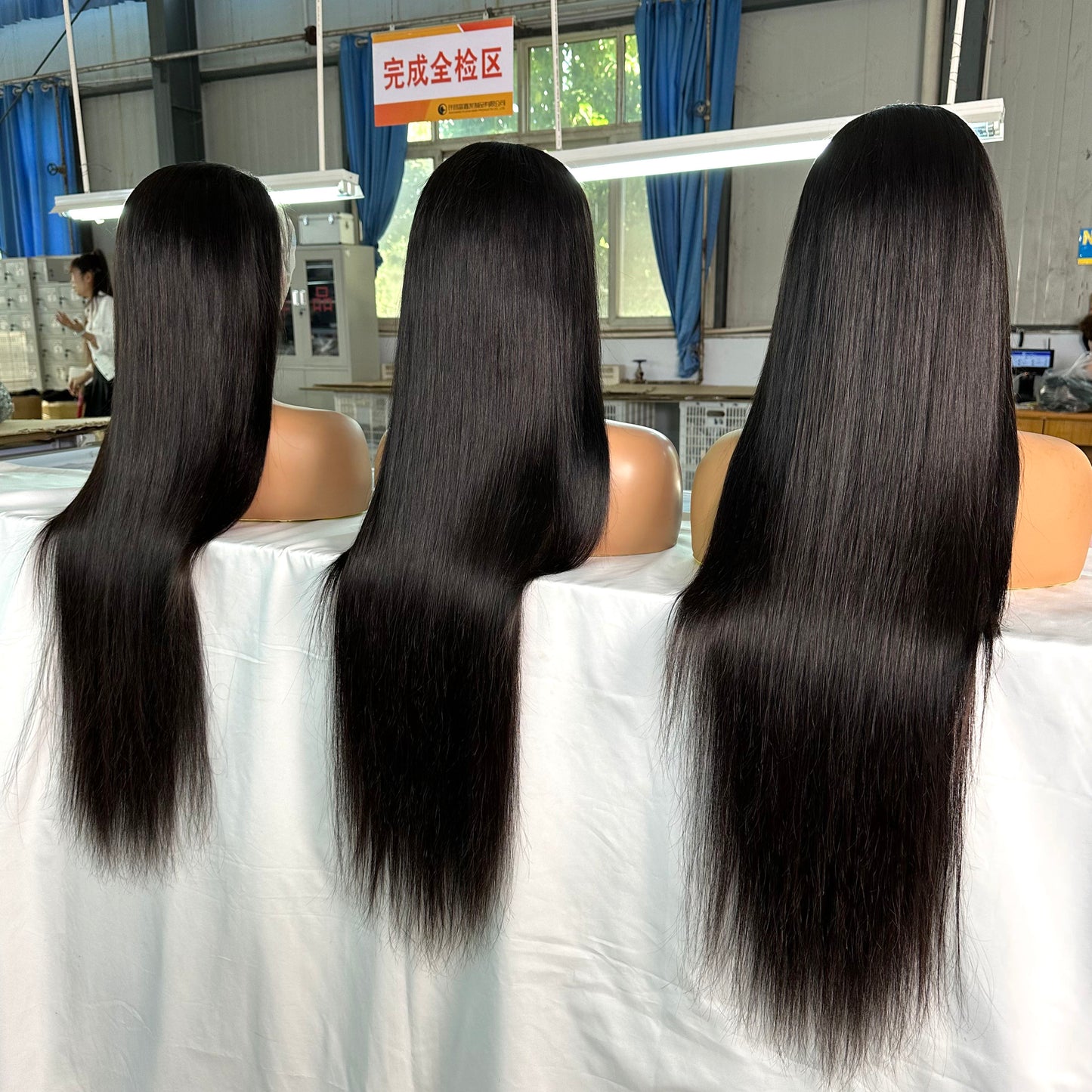 Three mannequin heads with long, straight black hair displayed in a bright workshop setting