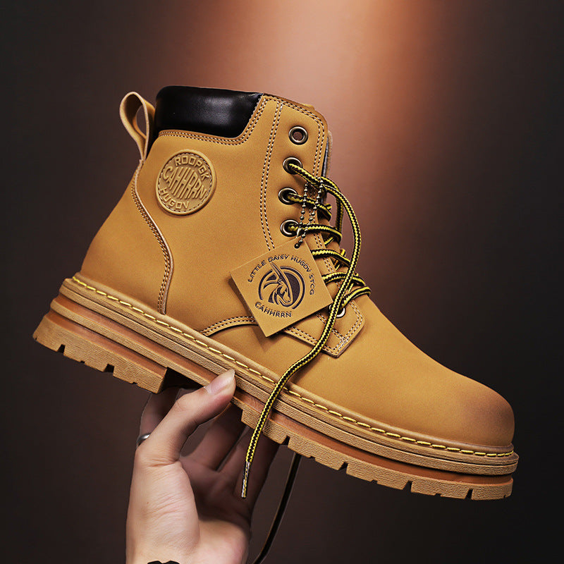 Hand holding tan leather work boot with black collar, branded patch, and yellow laces on brown background