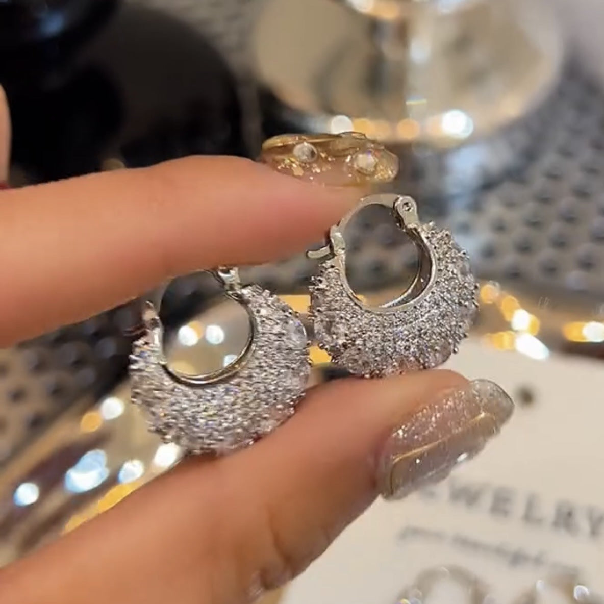 Hand holding silver hoop earrings encrusted with small sparkling diamonds